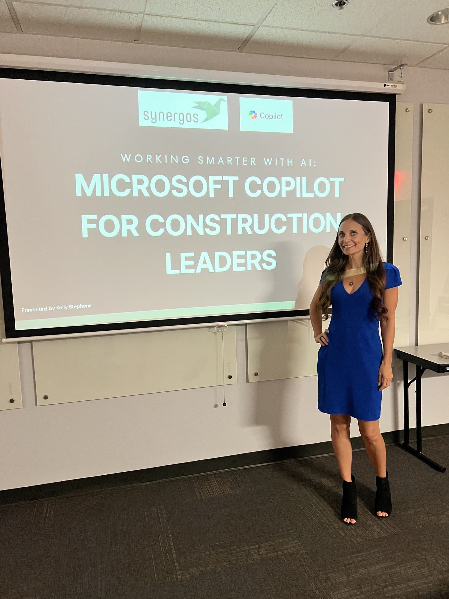 Kelly Stephens presenting her "Working Smarter with AI: Microsoft Copilot for Construction Leaders" training session, standing beside the projected title slide